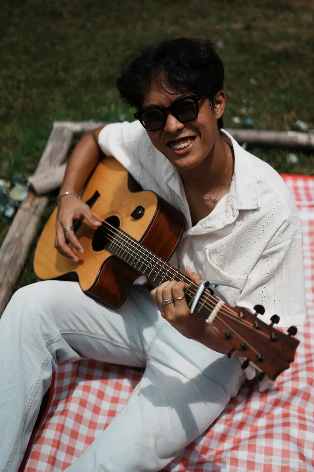 Julius smiling in sunglasses while holding an acoustic guitar on a picnic blanket.