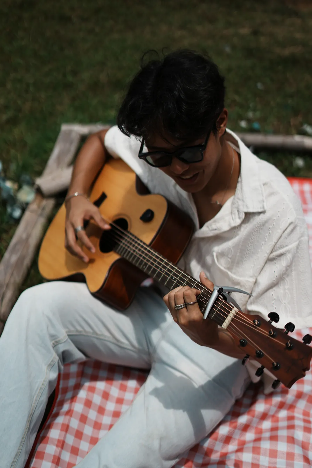 Julius looking down at an acoustic guitar during an outdoor picnic shoot.