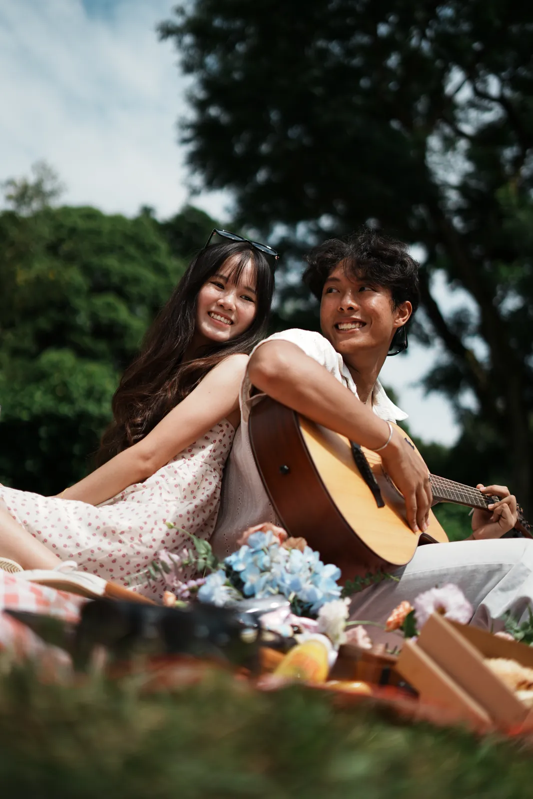 Julius and another model sitting back to back on a picnic blanket with a guitar.