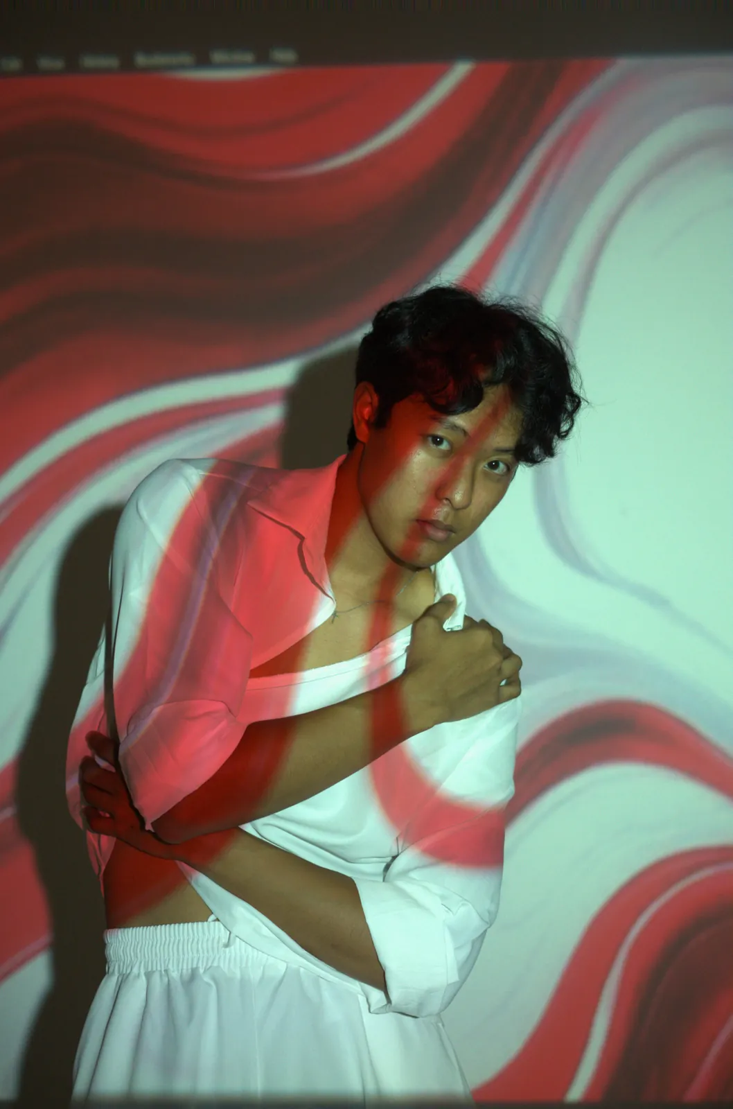 Julius in a white shirt with red and green patterns projected across his face and clothing.