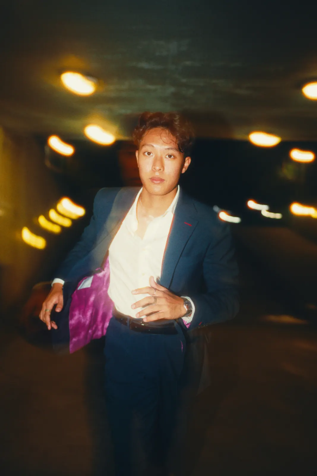 Julius in a dark blue suit beneath warm ceiling lights, photographed through soft motion blur.