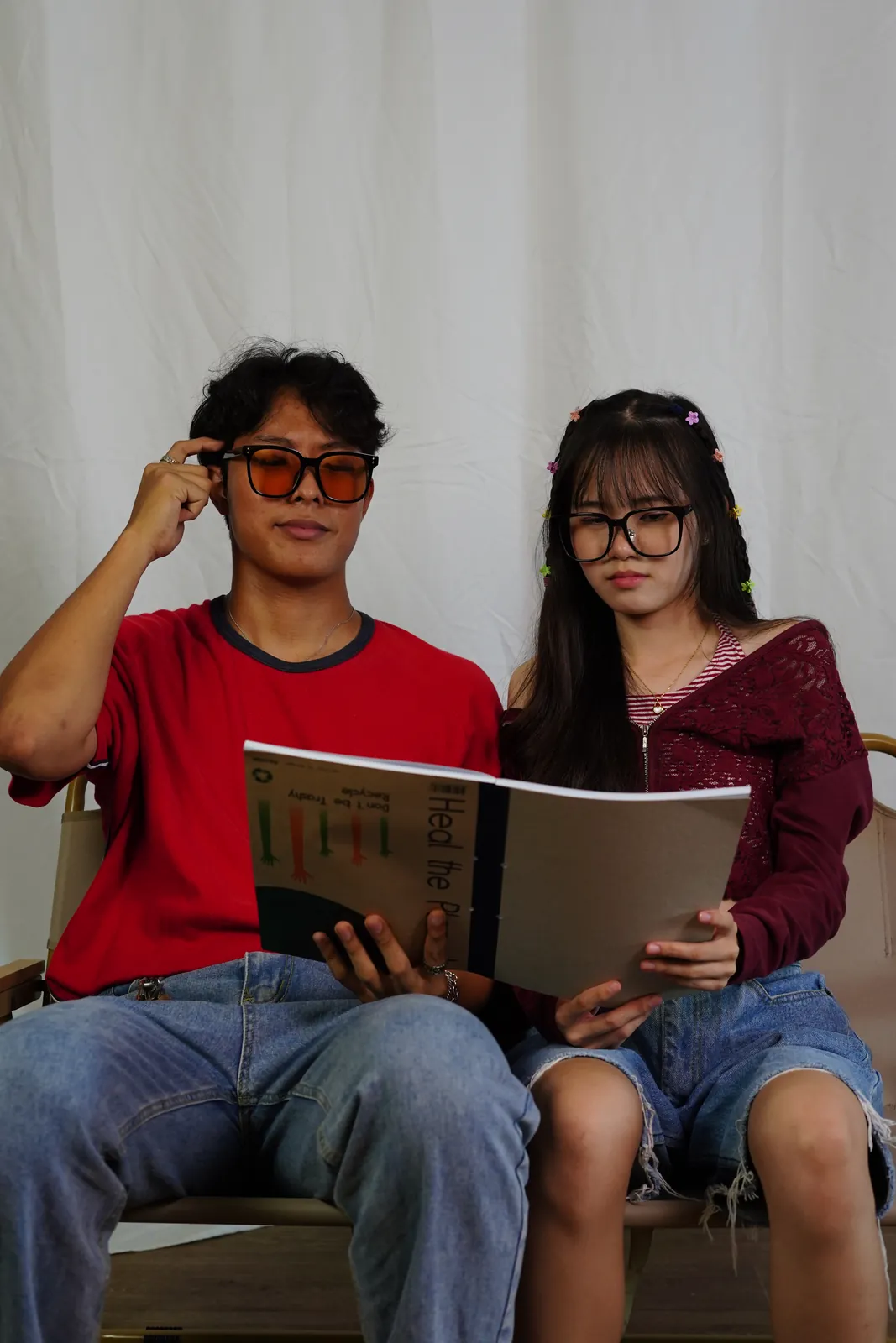 Julius in tinted glasses and another model reading a newspaper in a white studio.