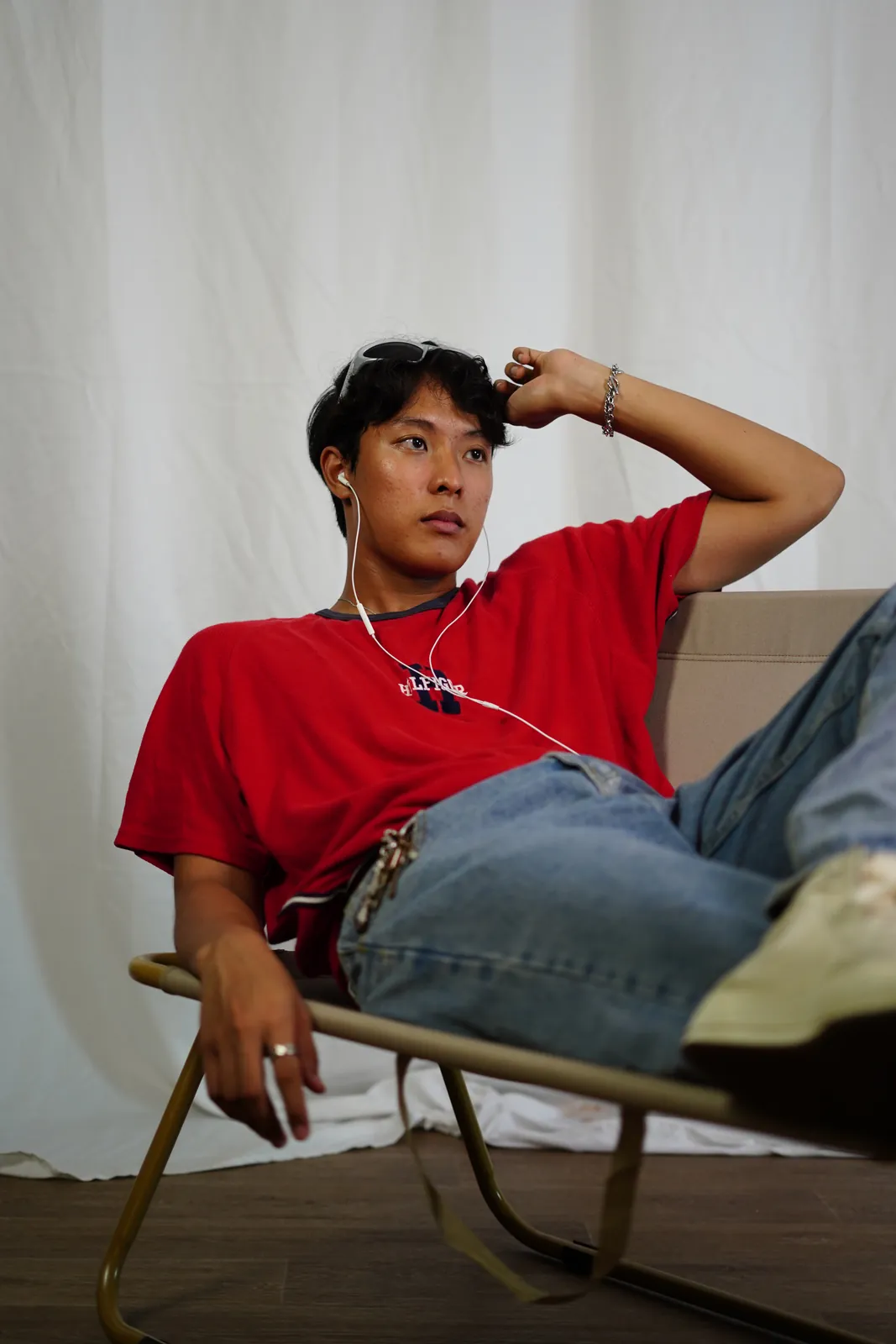 Julius reclining in a chair in a red shirt against white studio curtains.