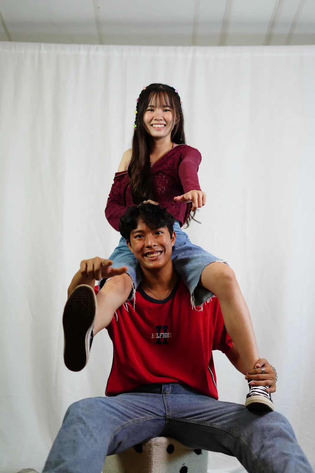 Julius seated in a red shirt with another model standing behind him, both laughing.