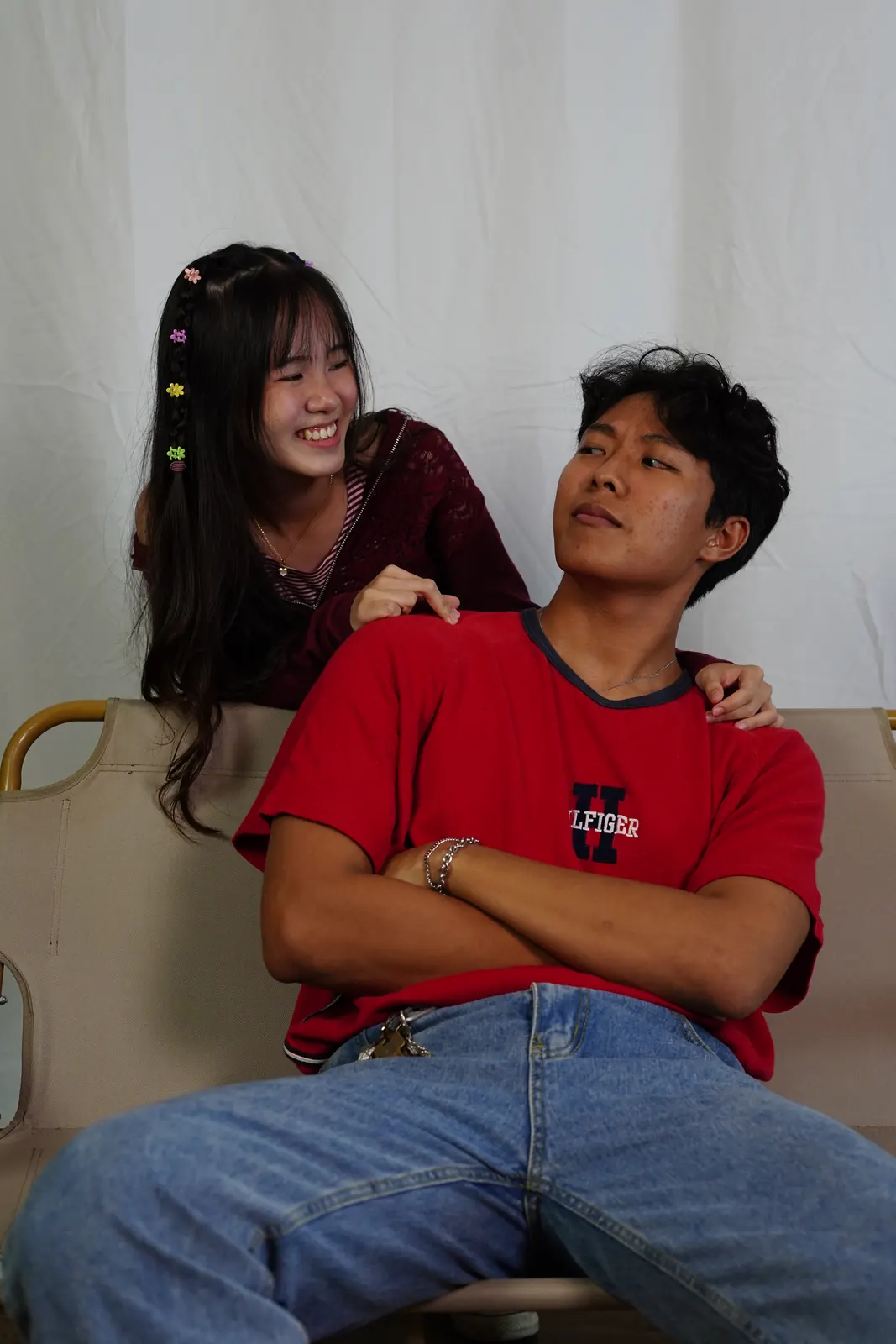 Julius seated in a red shirt while another model leans over his shoulder against a white backdrop.