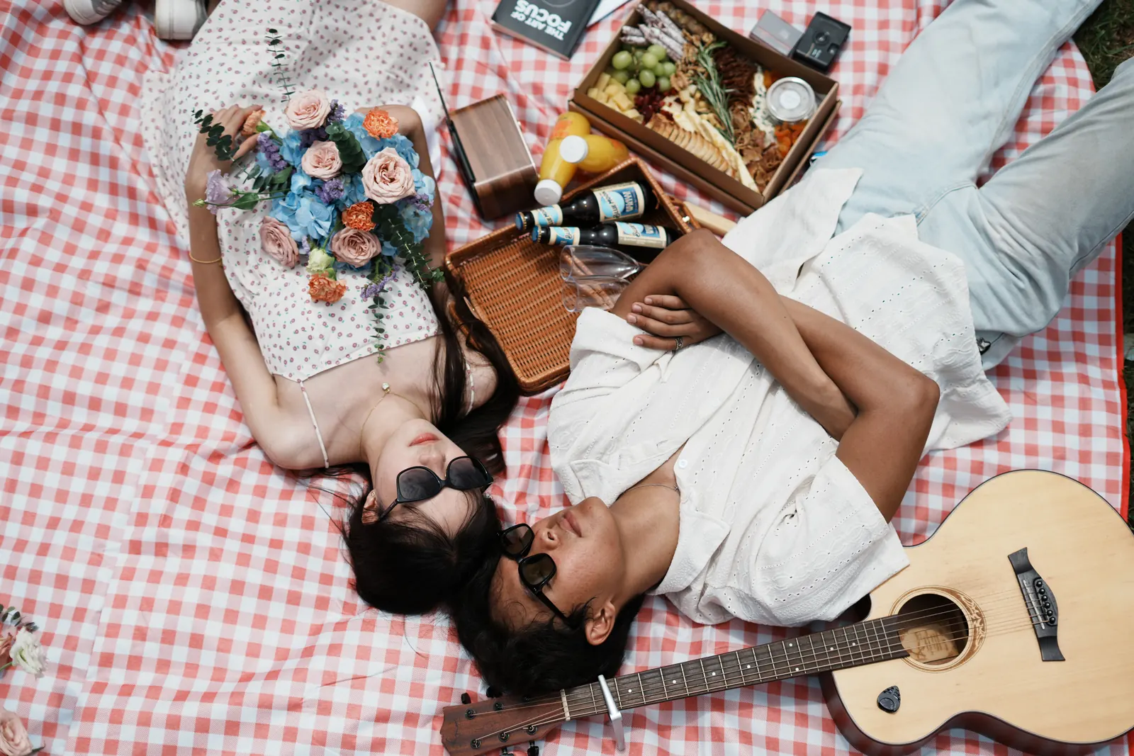 Overhead view of Julius and another model lying on a picnic blanket beside a guitar and flowers.