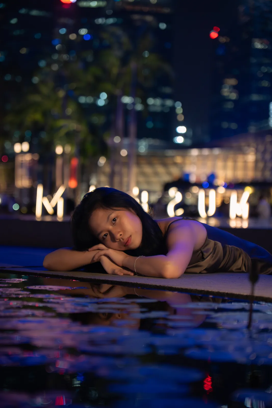 Woman resting her head on folded arms beside colourful night-time reflections.