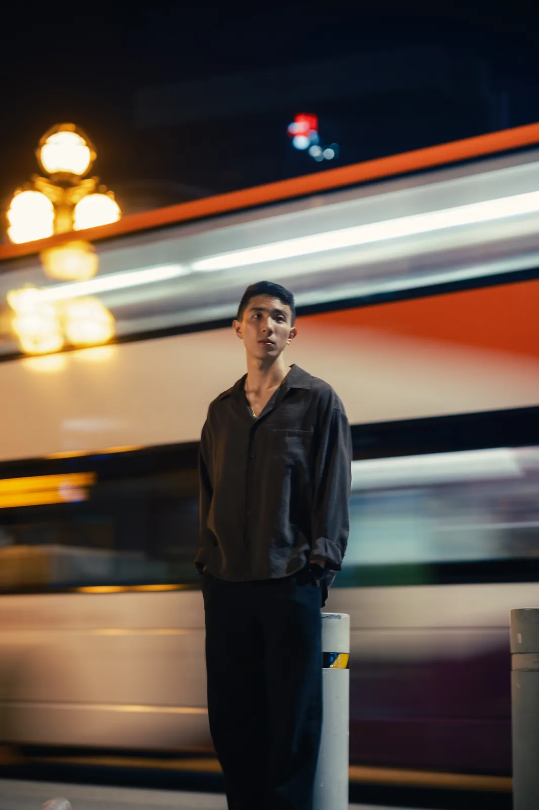 Man standing at night as a passing bus leaves streaks of light behind him.