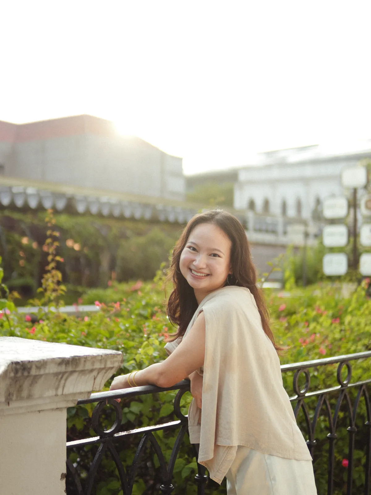 Woman smiling over her shoulder on a sunlit balcony overlooking greenery.