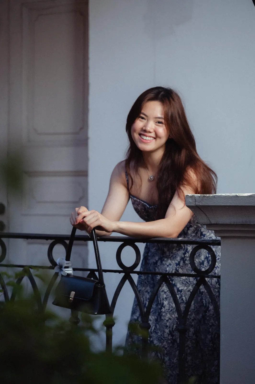 Smiling woman in a floral dress leaning against a railing in front of pale stone columns.