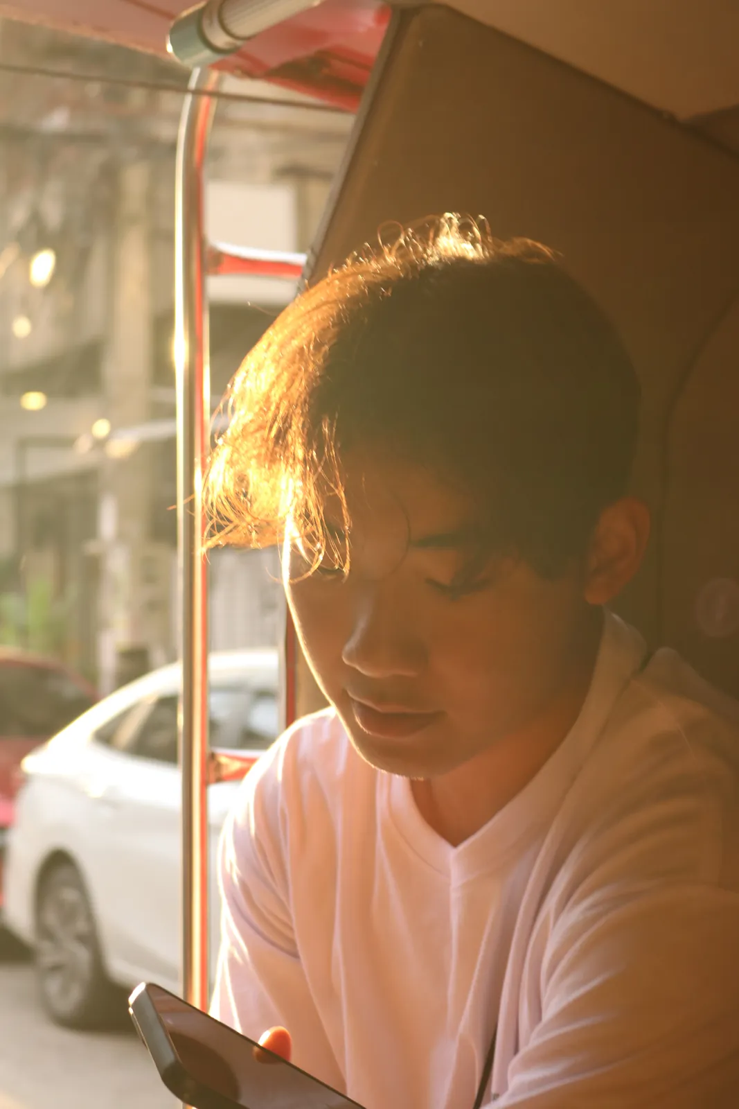 Man in a white shirt looking down in warm sunlight beside a street window.