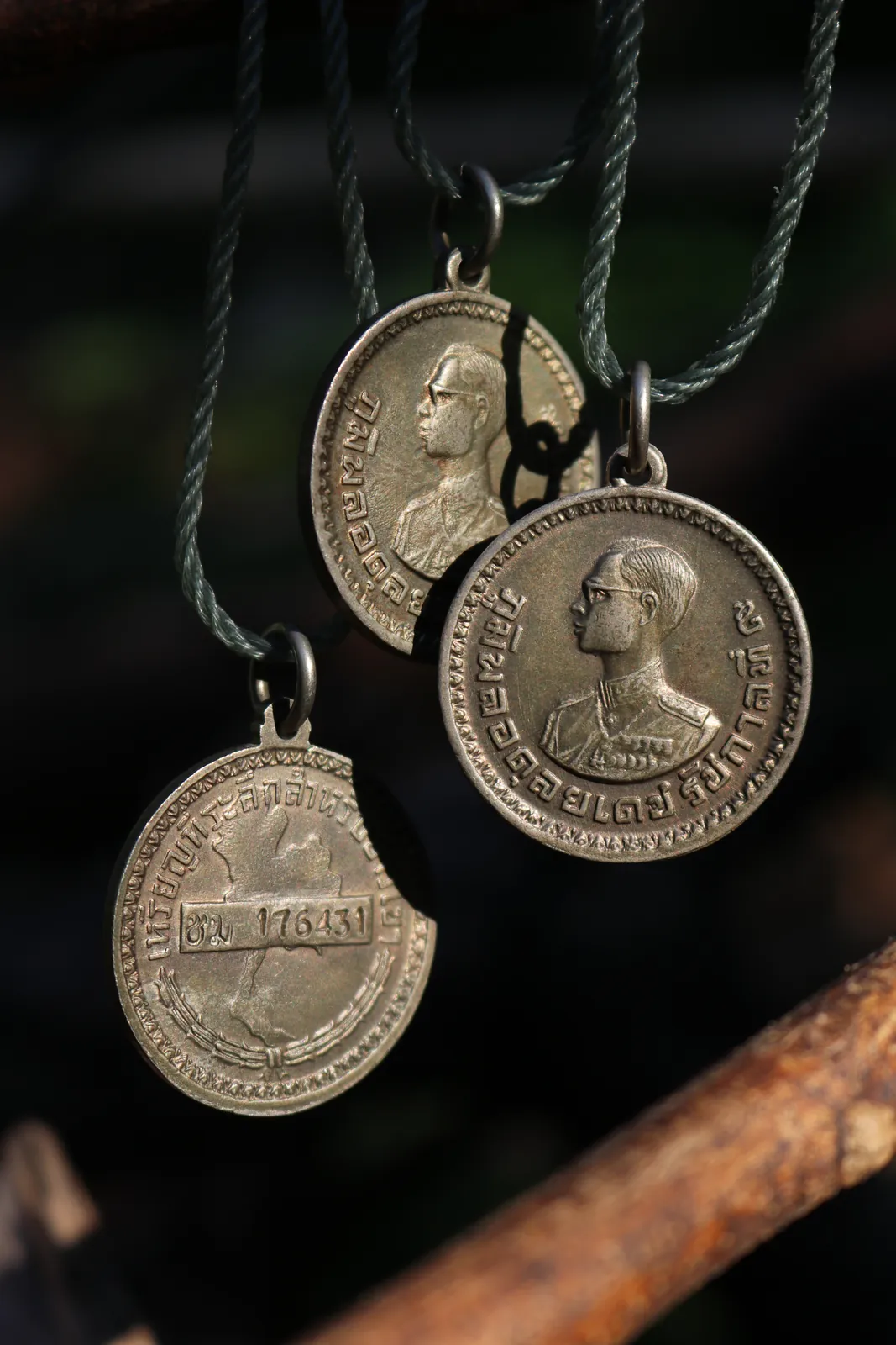 Three coin pendants suspended from dark cords against a shadowy background.